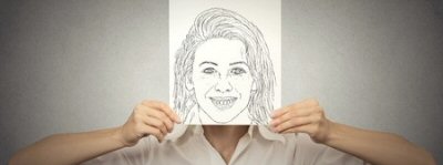 A person holding a drawing of a smiling face in front of their own face.