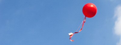 A bright red balloon floating away in a clear blue sky.