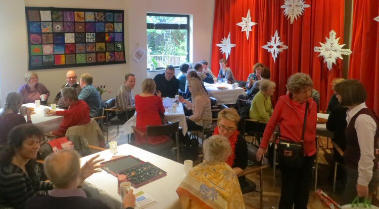 The church hall, full of people sitting round tables drinking cups of tea and coffee, engaging in conversation.